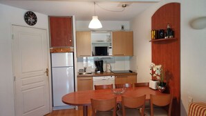 Cocina compacta con armarios de madera, un refrigerador blanco, un microondas y un lavamanos. Hay una mesa de comedor con cuatro sillas y una lámpara colgante sobre ella.