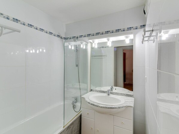 A modern bathroom with a glass-enclosed shower, a white sink with a marble countertop, and a large mirror above the sink.