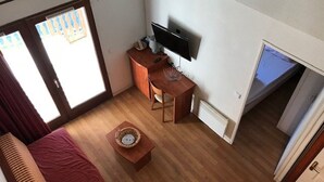 Una habitación con una cama, un escritorio, un televisor y una puerta corrediza a un balcón.