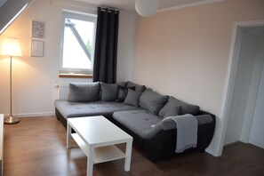 Ein modernes Wohnzimmer mit einem grauen Ecksofa, einem weißen Couchtisch und einer Stehlampe.