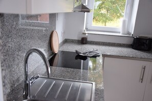 Eine Küche mit Granit Arbeitsplatten, einer schwarzen Kochplatte, einer Edelstahl-Spüle und einem Fenster mit Blick auf Bäume.