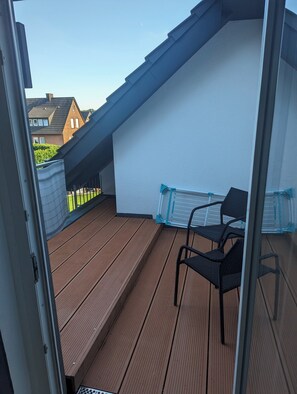Ein Balkon mit Holzboden, einem Stuhl und einer weißen Wand.