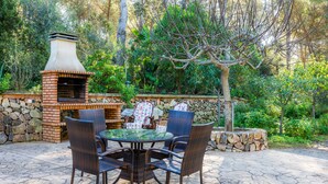Un patio al aire libre con una parrilla de ladrillo, sillas de mimbre y un muro de piedra.