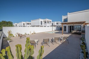A modern outdoor patio with a pool, lounge chairs, and cacti.