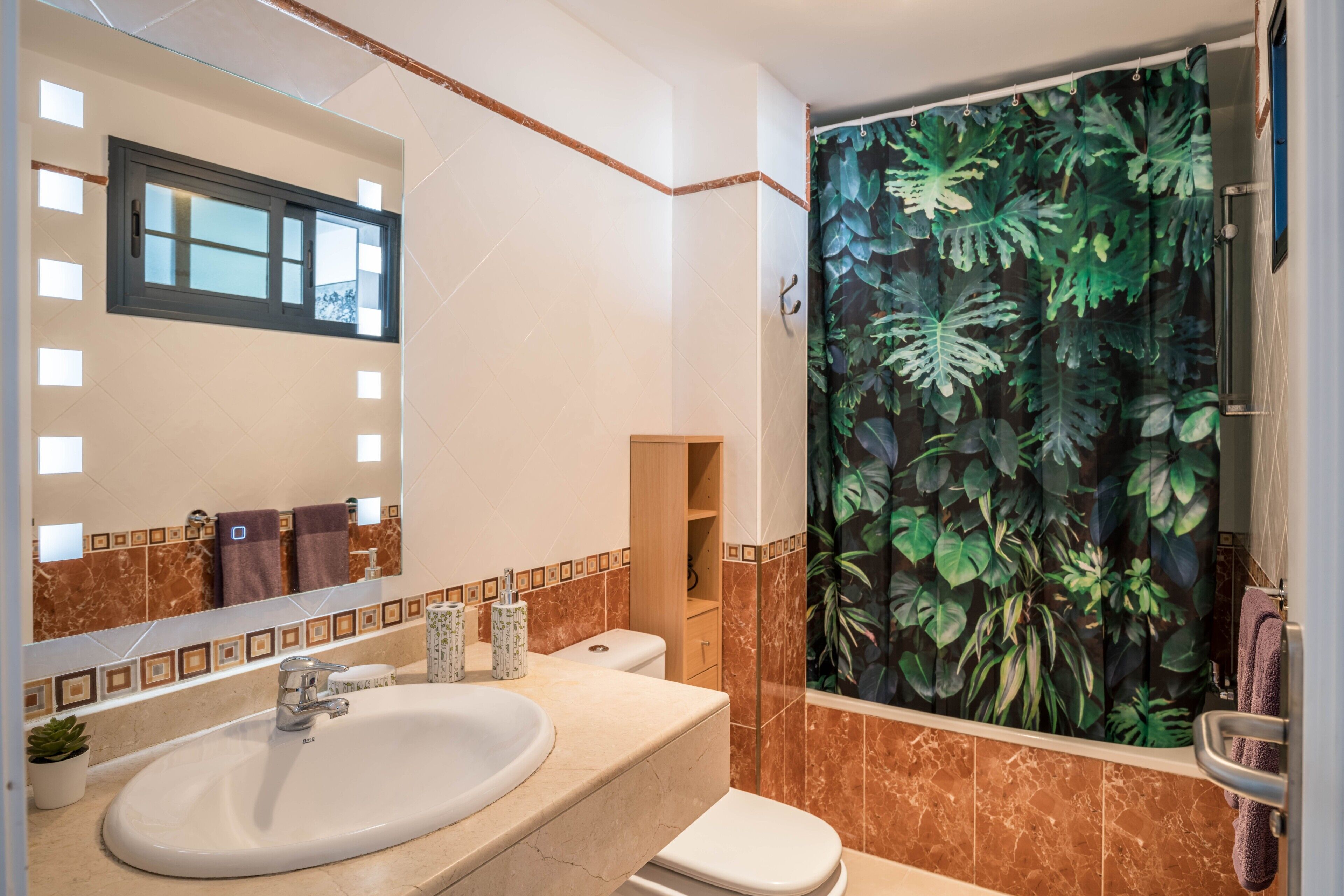 Un baño con lavamanos, inodoro y cortina de ducha estampada con hojas.