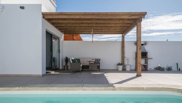 A poolside area with a pergola, outdoor seating, and a barbecue grill.