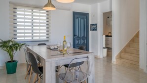 A dining area with a wooden table, chairs, pendant lights, a potted plant, and a blue door.