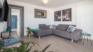 A modern living room with a grey sectional sofa, a flat-screen TV, a small table, and a potted plant.