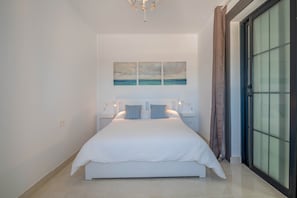 Une chambre à coucher avec un lit, des tables de chevet, un tableau et une vue à travers une porte vitrée.