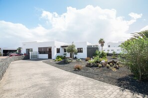 Un edificio moderno con vialetto lastricato, un piccolo giardino con diverse piante e cielo sereno.