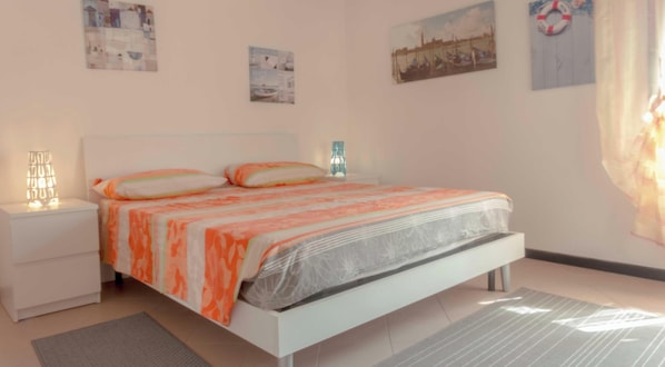 Quarto com cama, mesa de cabeceira, luminária e obra de arte na parede.