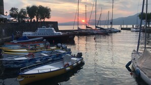 Ein Yachthafen mit verschiedenen vertäuten Booten, im Hintergrund ein Sonnenuntergang und eine Steinmauer an einer Seite.