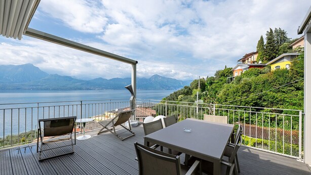 Eine Terrasse mit Tisch und Stühlen mit Blick auf einen See und Berge.
