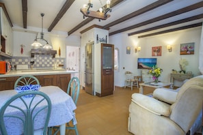 A kitchen with a dining area, wooden beams, a refrigerator, and a dining table with chairs.