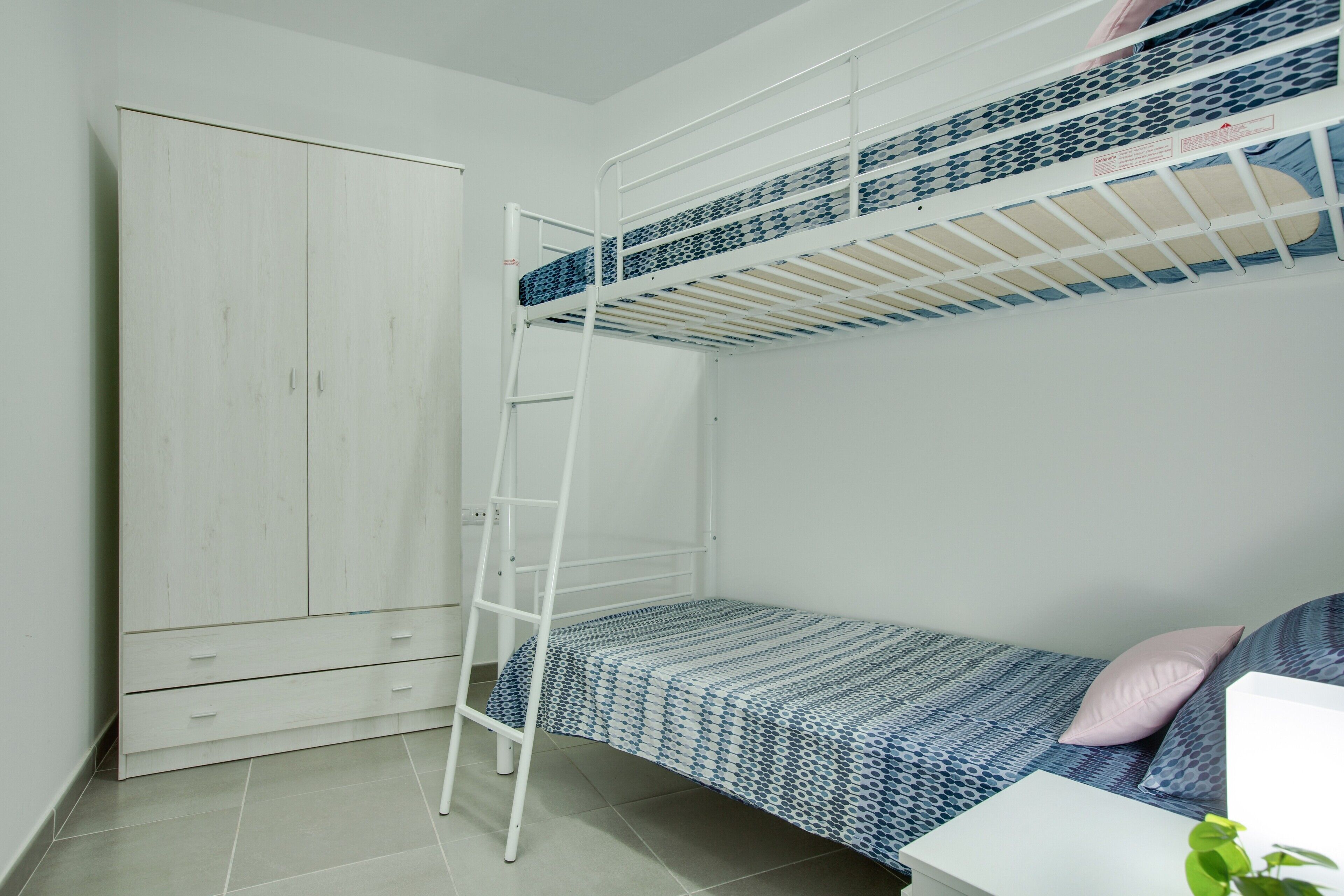 Una cama litera con escalera, un armario blanco y una mesita de noche con una planta.