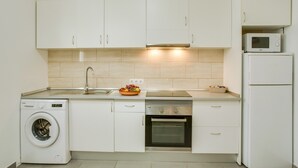 Una cocina compacta con armarios blancos, lavadora, microondas y horno.