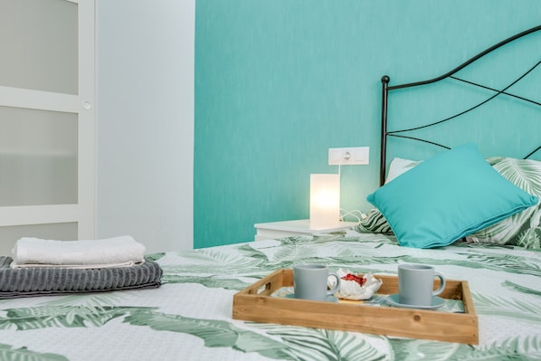 Un lit bien fait, avec un plateau contenant des articles pour le petit-déjeuner, une table de chevet avec une lampe et une fenêtre équipée de stores.