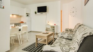 Una cocina moderna con armarios blancos, microondas y estufa. Hay un comedor con una mesa y sillas, y un salón con un sofá y televisor montado en la pared.