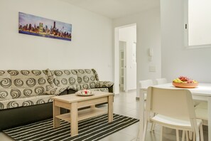 Un salon comprenant un canapé, une table basse, une table à manger avec des chaises et un panier de fruits.