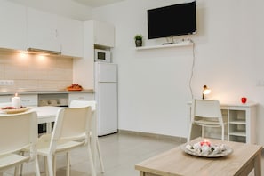 A modern kitchen with white cabinetry, a microwave, a refrigerator, and a dining area with a table and chairs.