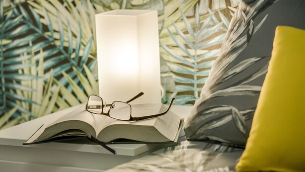 Una cama con un libro, gafas y una lámpara.