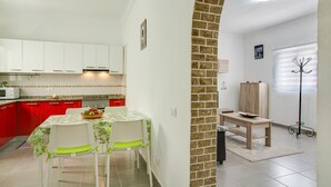 A kitchen with white cabinets, a dining table with chairs, and a brick wall. - Apartment “2A Francesca” close to the Sea with Wi-Fi & Fans (Vecindario)