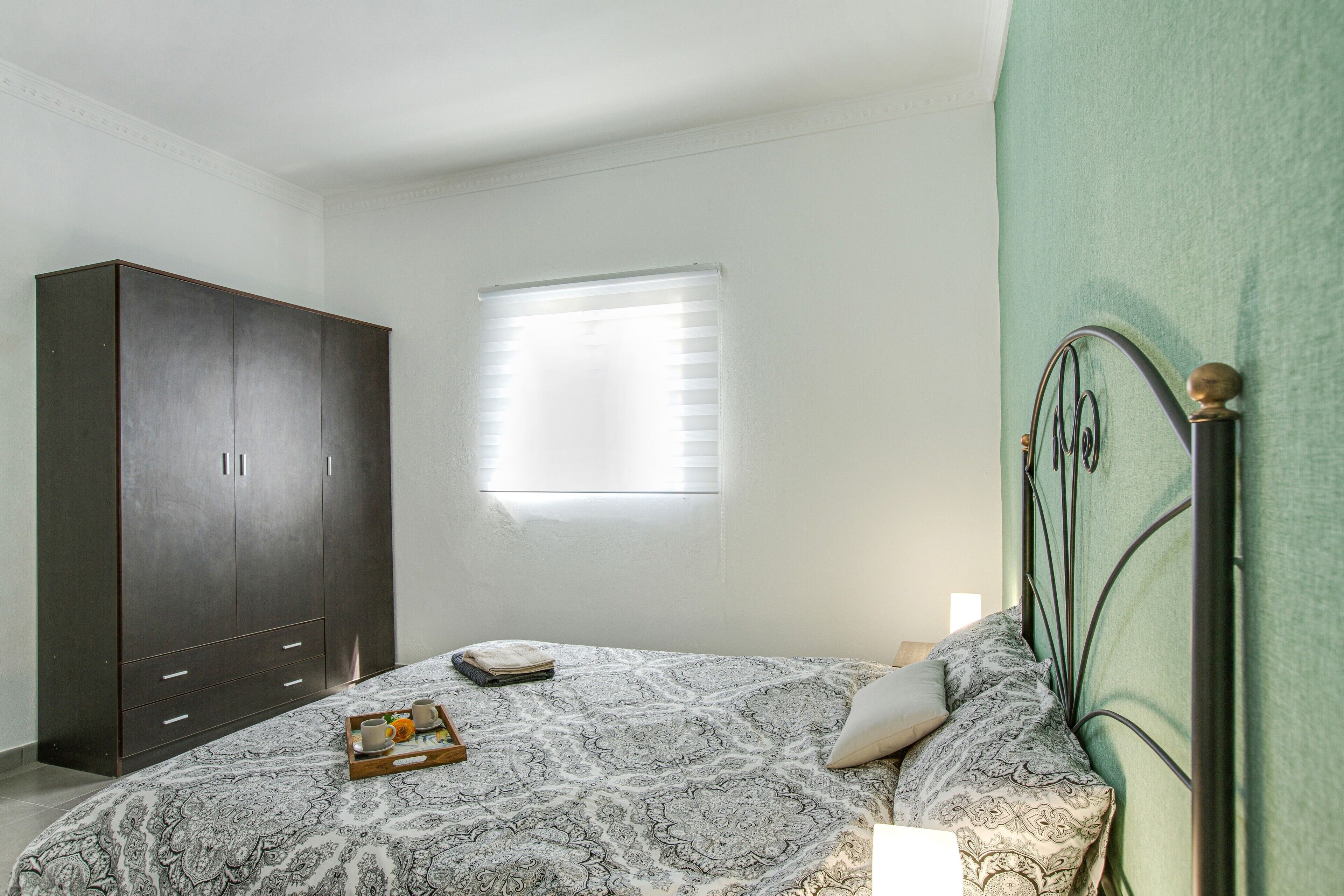 Une chambre à coucher avec un lit, une armoire, une fenêtre et un mur vert.