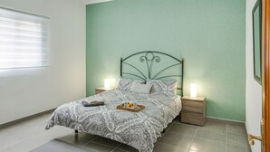 A bedroom with a bed, bedside tables, a nightstand, a window with blinds, and a green wall. - Apartment “2A Francesca” close to the Sea with Wi-Fi & Fans (Vecindario)