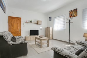 A living room with a sofa, a coffee table, a TV, and a coat rack.