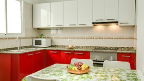 A kitchen with red cabinets, a microwave, and a fruit bowl on the table. - Apartment “2A Francesca” close to the Sea with Wi-Fi & Fans (Vecindario)