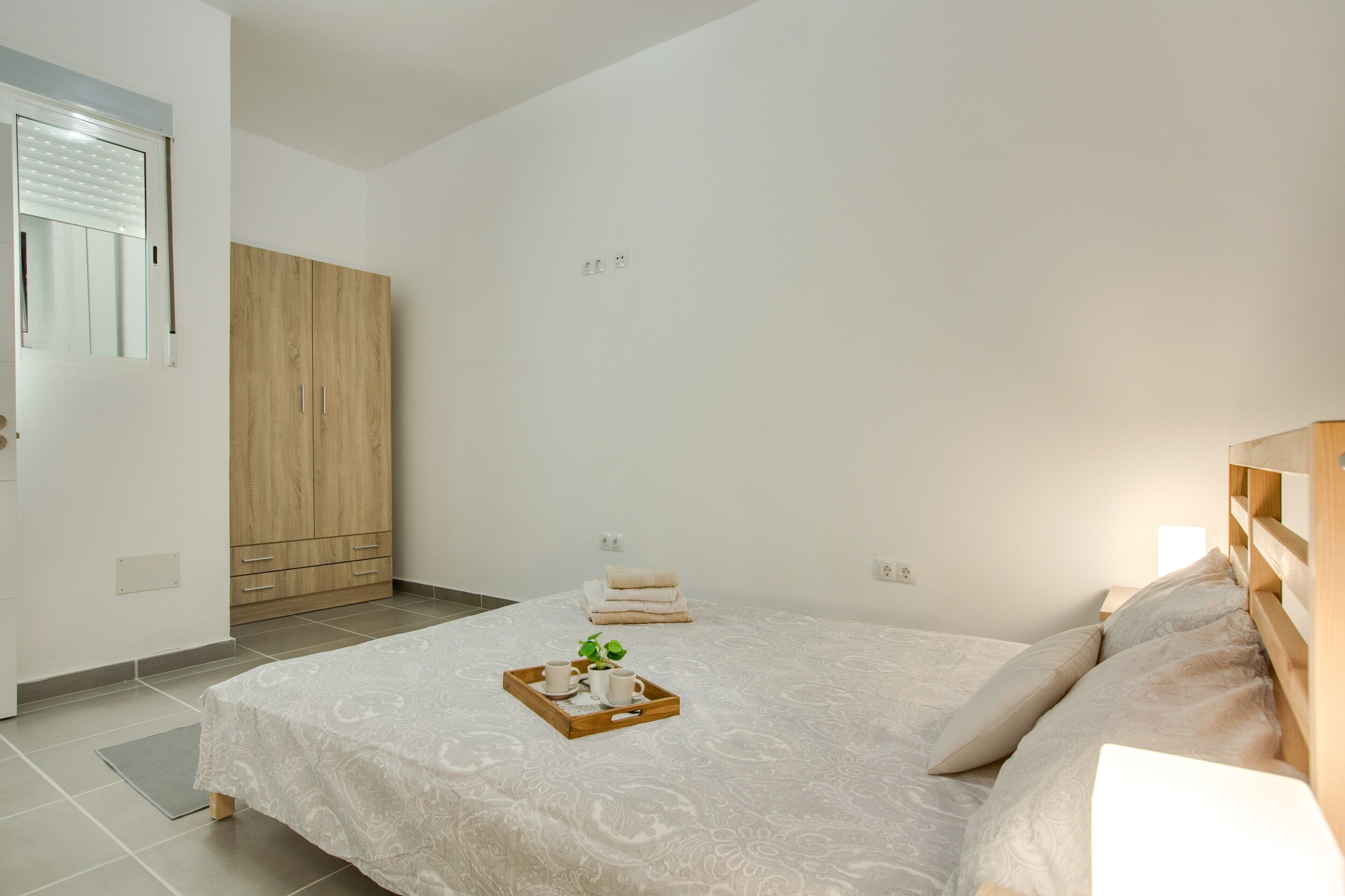 A bedroom with a bed, a wardrobe, a bedside table, and a tray with a plant.