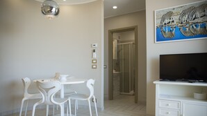 A modern dining area with a round table and white chairs, a white cabinet with a flat-screen TV, and a zebra painting on the wall.
