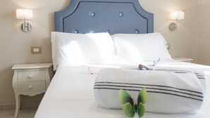 A hotel room with a bed, white bedding, a blue headboard, two bedside lamps, a nightstand with drawers, and a decorative pillow with a butterfly.
