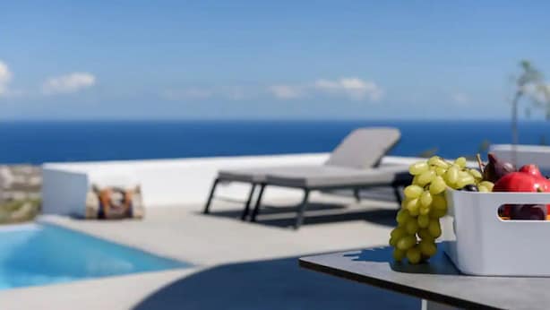 A poolside area with a lounge chair, a table with a fruit bowl, and a view of the ocean. - Salty villa with private Pool & Sea view (Santorini)