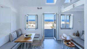 A modern, open-plan living space with a view of the sea, featuring a dining area, seating, and large windows. - Sandy villa with private pool & Sea view (Santorini)