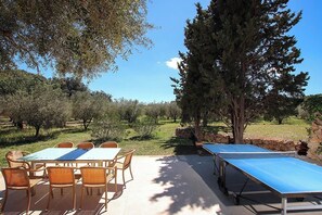 Enjoy dining or socializing in this serene outdoor space surrounded by lush trees and shrubs, featuring a table, chairs, and a ping pong table.