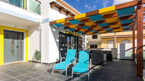 A covered outdoor area with blue lounge chairs, a green garden hose, and a tiled floor.