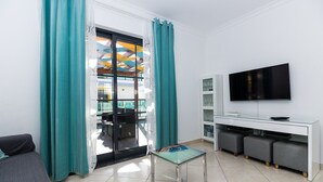 A modern living room with a sofa, a glass coffee table, a flat-screen TV, and a sliding glass door leading to an outdoor area.