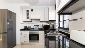 A modern kitchen with stainless steel appliances, white cabinetry, and a black granite countertop.