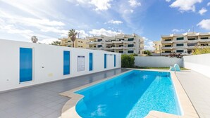 A swimming pool with a tiled deck, surrounded by a white wall with blue accents and a sign.