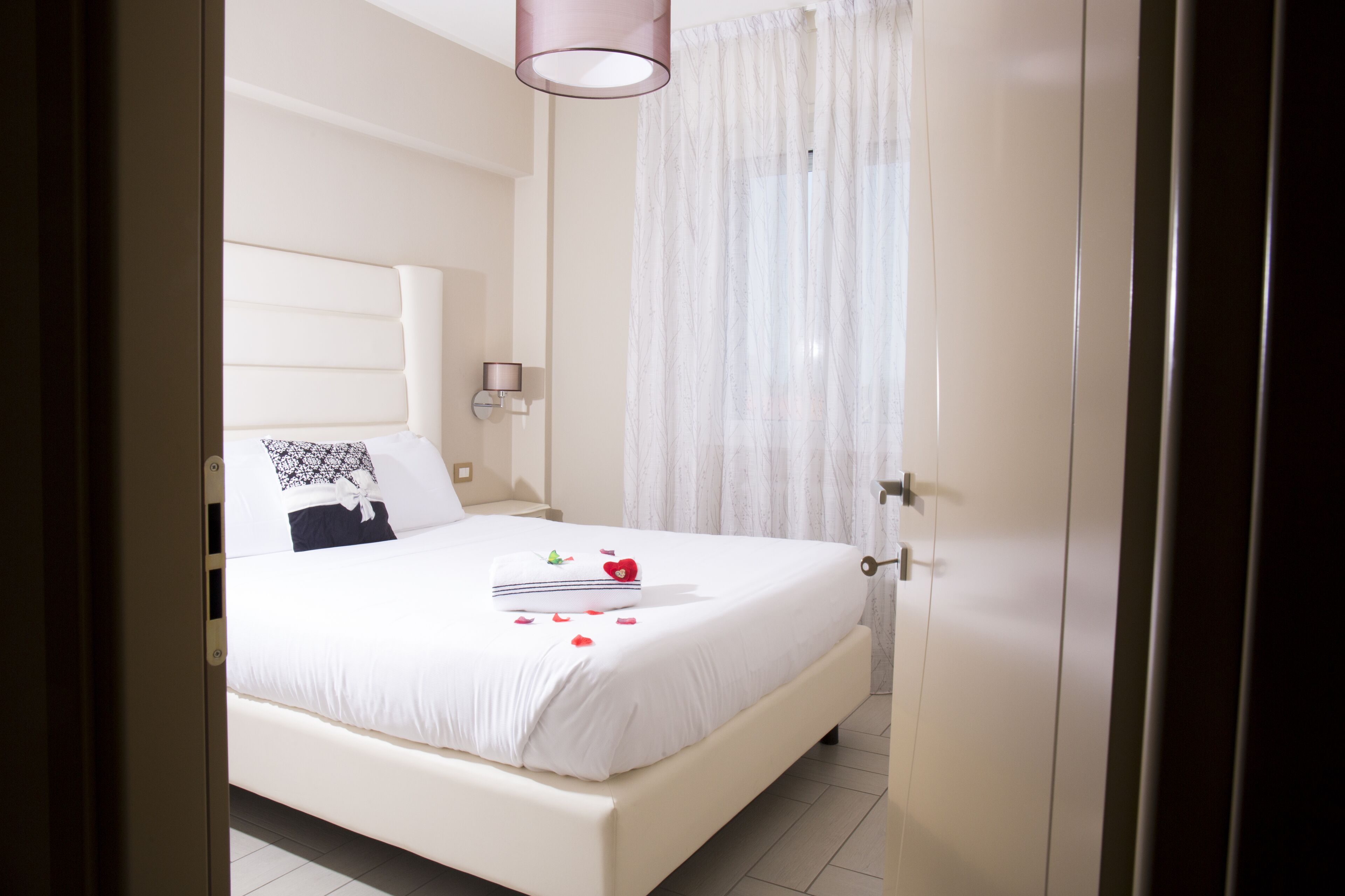 Un lit bien fait, avec une couette blanche, un coussin décoratif et un coussin en forme de cœur orné d’une rose.