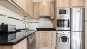 A modern kitchen with wooden cabinets, a built-in dishwasher, a stainless steel refrigerator, a microwave, and a washing machine.