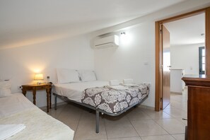 Ein Hotelzimmer mit einem Bett, einem Nachttisch mit Lampe, einer Klimaanlage und einer Tür zu einem weiteren Raum.