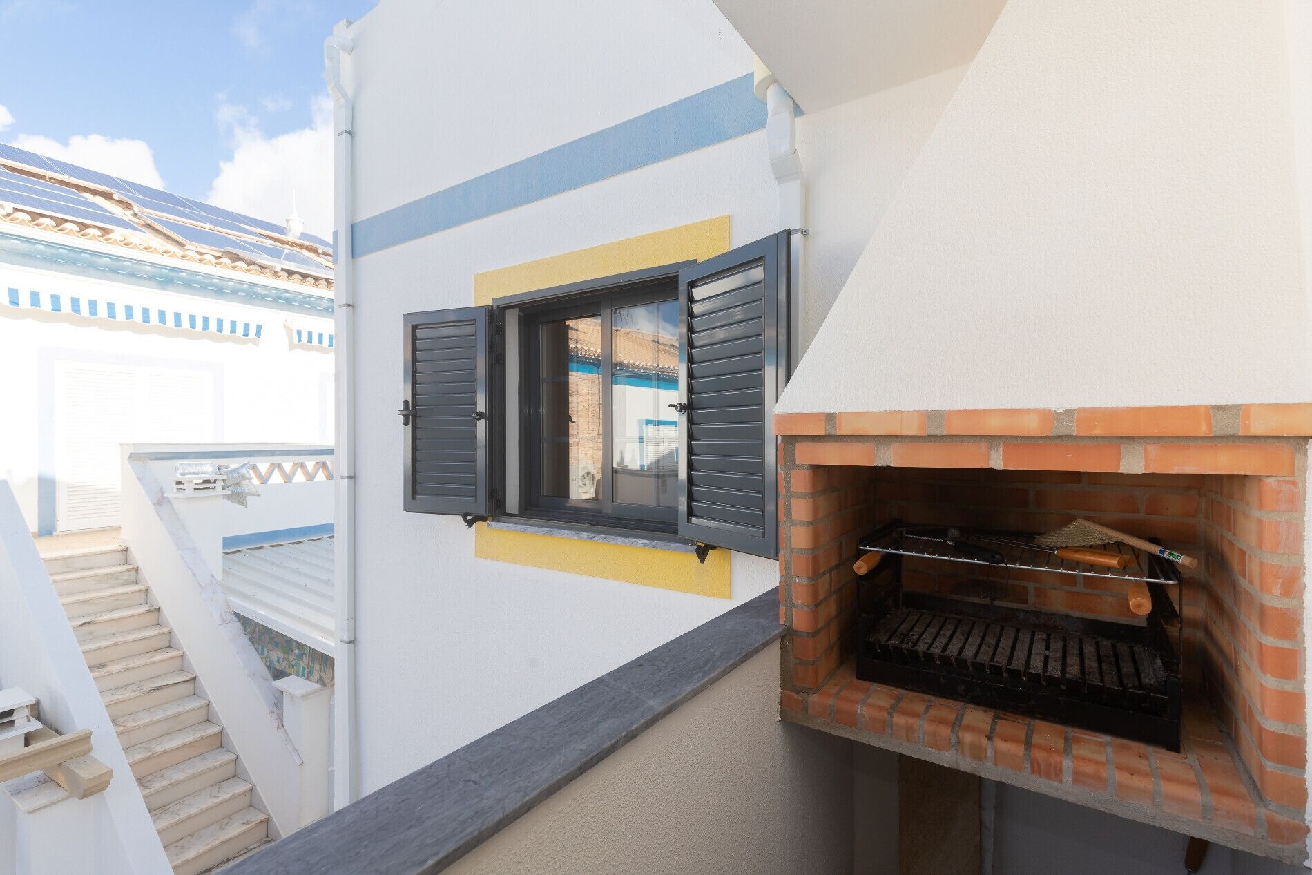 Un edificio residencial con chimenea de ladrillo, ventana con contraventanas y una escalera.