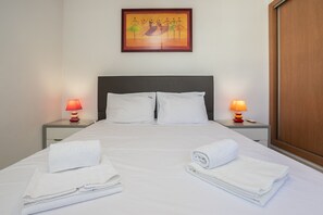 A hotel room with a bed, two bedside lamps, a painting on the wall, and a wooden wardrobe.