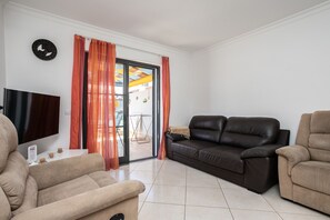 Ein Wohnzimmer mit einer Couch, Sesseln, einem Flachbildfernseher und einer Glastür zum Außenbereich.