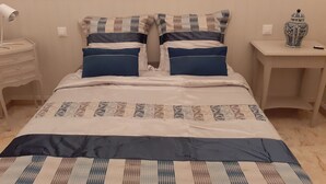 A neatly made bed with a patterned bedspread and two pillows, a bedside lamp, a small table with a vase, and a wall-mounted light fixture. - CASA DI MAMMA near gorges de L'ASCO corsican center, river, sea. (Moltifao)