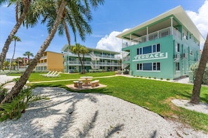A multi-story hotel with a green facade, a terrace area with seating, and palm trees.