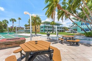 A courtyard with outdoor seating, palm trees, and a tennis court.