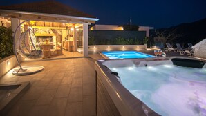 Ein Whirlpool, ein Schwimmbecken und ein überdachter Außenbereich mit Sitzgelegenheiten.